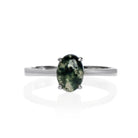 A product photo of an oval 925 sterling silver solitaire ring on a white background. The band is rounded and smooth, and the 7x5mm cabochon moss agate is held in place by 4 delicate silver claws.