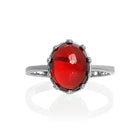 A product photo of a 925 sterling silver red garnet birthstone ring sitting on a white background. The garnet is impressively large, with the cabochon cut allowing the viewer to look into the stone like a crystal ball.  The 10x8mm oval stone is encased in ornate silver detailing, almost like a royal crown.