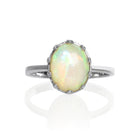 A product photo of a 925 sterling silver black Ethiopian opal birthstone ring sitting on a white background. The opal is impressively large, with the cabochon cut allowing the viewer to look into the stone like a crystal ball.  The 10x8mm oval stone is encased in ornate silver detailing, almost like a royal crown.