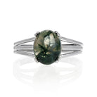 A product photo of a 925 sterling silver moss agate ring sitting on a white background. The moss agate is impressively large, with the cabochon cut allowing the viewer to see every detail of its swirling, ink-like dendritic inclusions. The bandsplits into three prongs on either side of the stone.