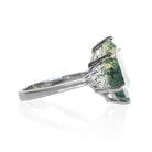 A product photo of a statement moissanite and moss agate engagement ring in solid 925 sterling silver sitting on a white background. The band is smooth and rounded. The impressively large 14x10mm Hexagonal Moss Agate gemstone is embraced on either side by a delicate trio of bright white moissanite gems.