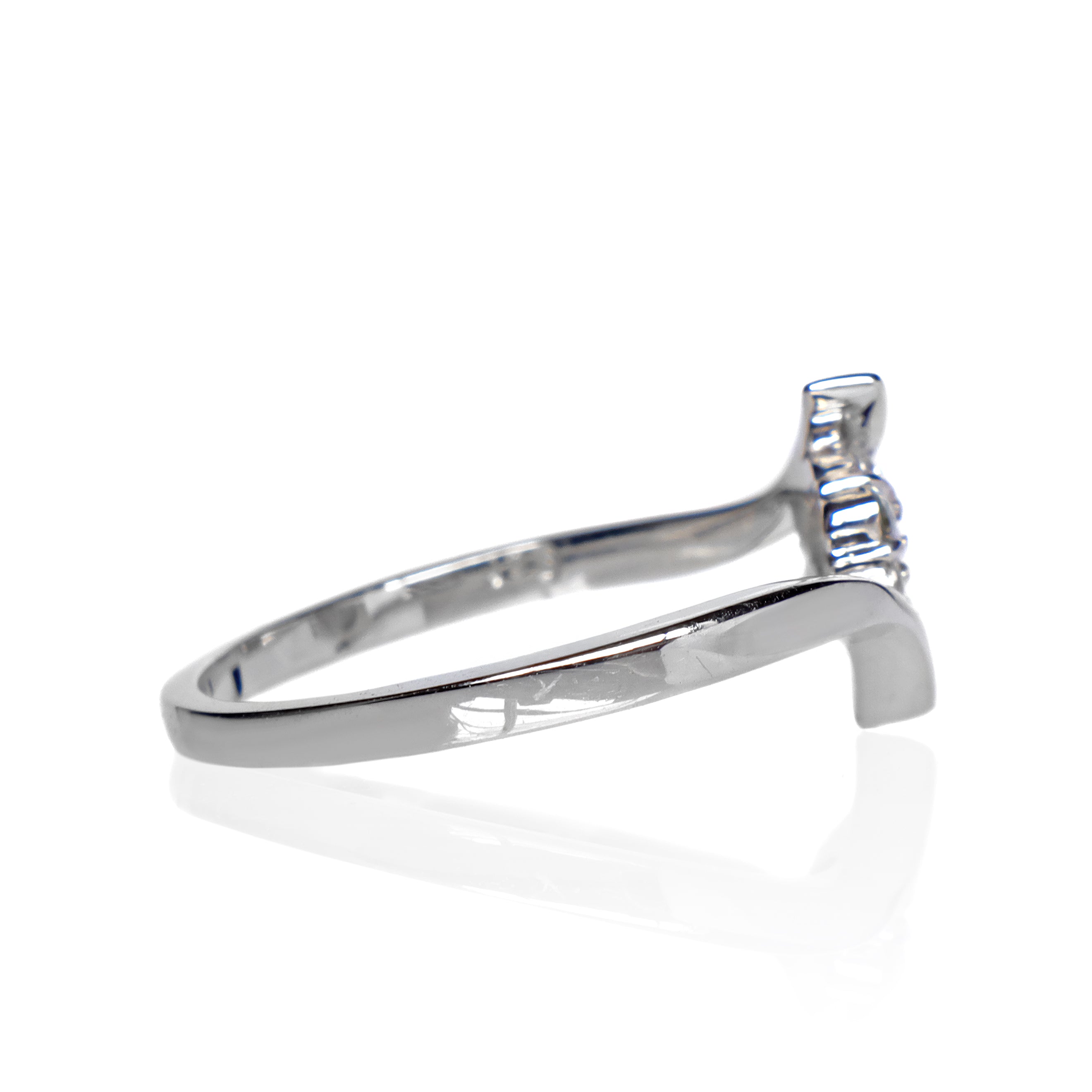 A product photo of a moissanite ring in 9k white gold on a clear white background. A simple crescent band hugs the top and bottom of the 7-jewel cluster of reflective moissanite gems in the centre.