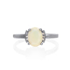 A product photo of a silver black and white ethiopian rainbow opal and moissanite trio ring sitting on a white background. The oval, opaque-cream ethiopian rainbow opal gemstone stands in stark contrast to the little clusters of three classic white moissanite stones on either side.