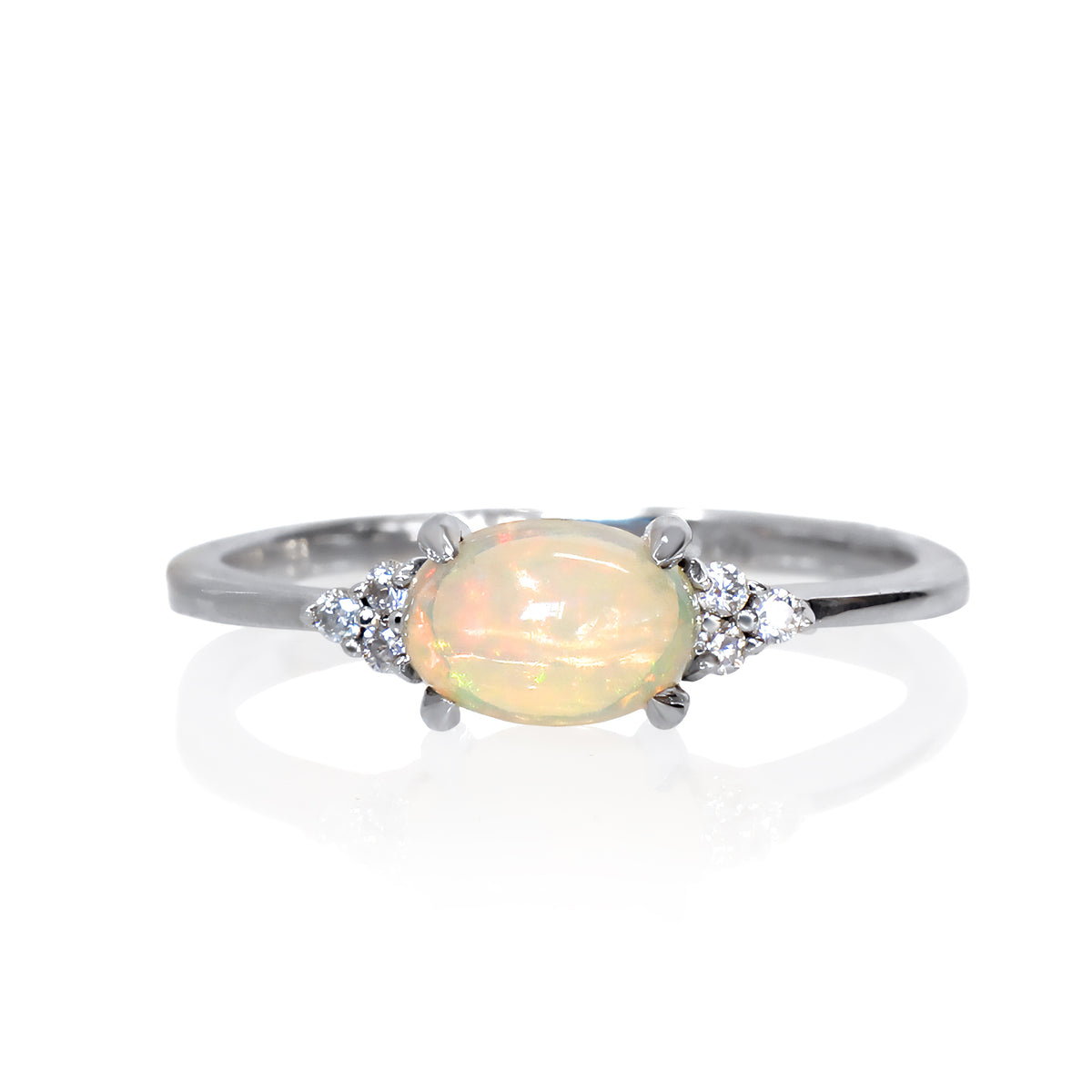 A product photo of a silver Ethiopian rainbow opal and moissanite ring sitting against a white background. The silver band is plain and smooth, and the horizontally-oriented cabochon Ethiopian rainbow opal centre stone is framed by a delicate trio of moissanite on either side.