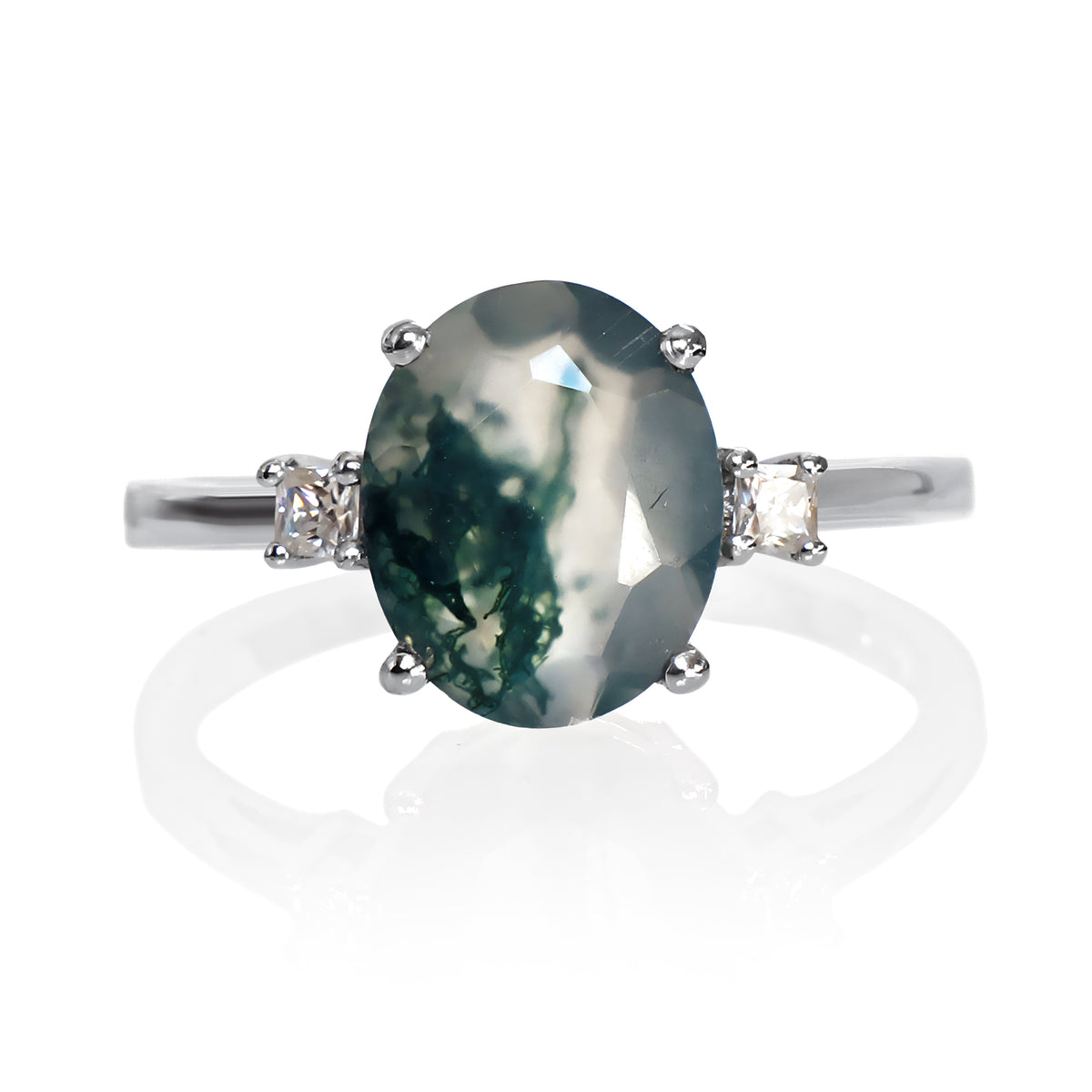 A product photo of a sterling silver ring with a large, 10x8mm oval green moss agate center stone. The agate displays unique moss-like inclusions and is secured by four prongs. It is flanked on each side by a small, square-cut white moissanite stone, all set on a polished band against a white background, with a soft reflection visible below.