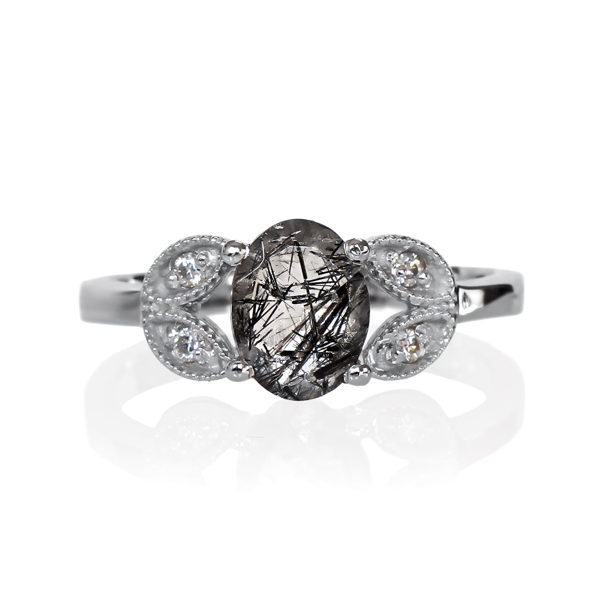 A product photo of an oval tourmalated quartz and moissanite ring with floral silver detailing set in solid 925 sterling silver metal. The bold 8x6mm tourmalated quartz gemstone is held in place by two petal shapes in filigree silver detailing on either side, each "petal" adorned with a single moissanite in the centre, to a total of 4.
