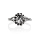 A product photo of a lavish floral moissanite halo tourmalated quartz ring in solid silver on a white background. The smooth band splits in two halfway along its length on either side, meeting the floral halo and tourmalated quartz in the centre. The tourmalated quartz centre stone is held in place by 4 claws and is lightly included, with natural black strikes snaking throughout the monochromatic jewel.
