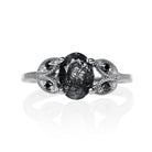 A product photo of an oval tourmalated quartz and black moissanite ring with floral silver detailing set in solid 925 sterling silver metal. The bold 8x6mm tourmalated quartz gemstone is held in place by two petal shapes in filigree silver detailing on either side, each "petal" adorned with a single black moissanite in the centre, to a total of 4.