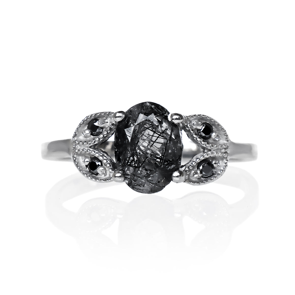 A product photo of an oval tourmalated quartz and black moissanite ring with floral silver detailing set in solid 925 sterling silver metal. The bold 8x6mm tourmalated quartz gemstone is held in place by two petal shapes in filigree silver detailing on either side, each "petal" adorned with a single black moissanite in the centre, to a total of 4.