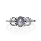 A product photo of a silver grey moonstone ring on a white background. The ring consists of a single 7x5mm cabochon-cut moonstone stone hugged between two looping silver "petals" on either side, which transition into a smooth flat band in the middle.