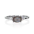 A product photo of a silver grey moonstone and moissanite ring sitting against a white background. The silver band is plain and smooth, and the horizontally-oriented cabochon moonstone centre stone is framed by a delicate trio of moissanite on either side.