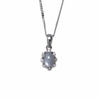 A product photo from  showing a silver moonstone pendant on a fine twist chain against a white background. The moonstone is secured by four discreet claws and surrounded by a scalloped, floral-inspired halo set with small, glittering white accent stones. The pendant hangs from a polished, classic tapered silver bail.
