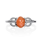 A product photo of a silver orange moonstone ring on a white background. The ring consists of a single 7x5mm cabochon-cut moonstone stone hugged between two looping silver "petals" on either side, which transition into a smooth flat band in the middle.