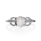 A product photo of a silver moonstone ring on a white background. The ring consists of a single 7x5mm cabochon-cut moonstone stone hugged between two looping silver "petals" on either side, which transition into a smooth flat band in the middle.