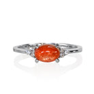 A product photo of a silver sunstone and moissanite ring sitting against a white background. The silver band is plain and smooth, and the horizontally-oriented cabochon sunstone centre stone is framed by a delicate trio of moissanite on either side.
