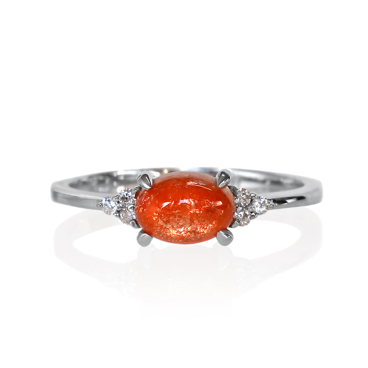 A product photo of a silver sunstone and moissanite ring sitting against a white background. The silver band is plain and smooth, and the horizontally-oriented cabochon sunstone centre stone is framed by a delicate trio of moissanite on either side.
