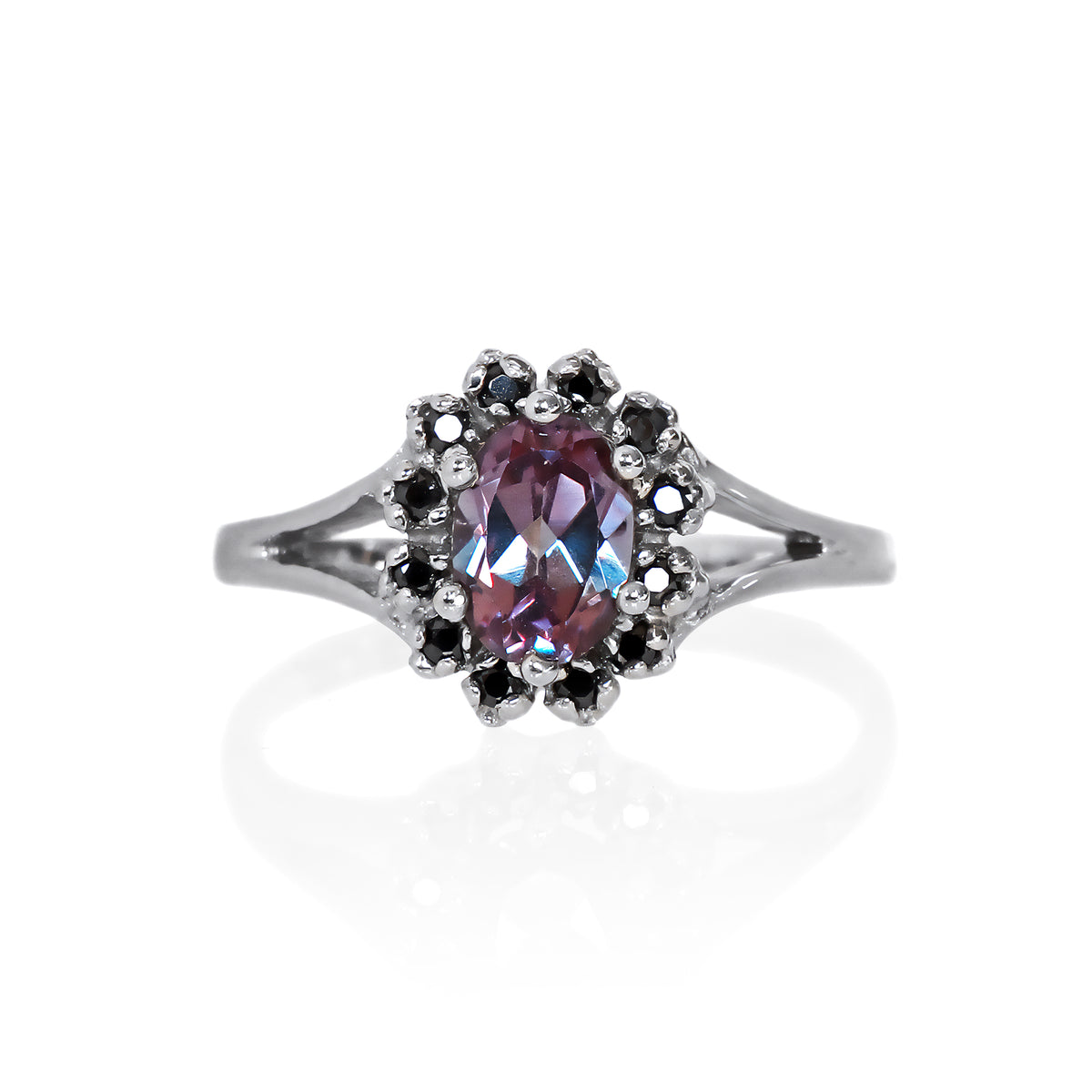A product photo of a lavish floral moissanite halo lab alexandrite ring in solid silver on a white background. The smooth band splits in two halfway along its length on either side, meeting the floral halo and lab alexandrite in the centre. The lab alexandrite centre stone is held in place by 4 claws and is lightly included, with natural black strikes snaking throughout the monochromatic jewel.