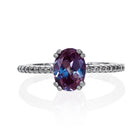 A product photo of a silver lab alexandrite engagement ring on a white background. The ring draws from contemporary alternative styling with the 8x6mm lab alexandrite centre stone, while calling back to the pavÃ© engagement styles of the past with its moissanite-embedded band.