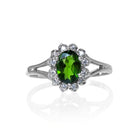 A product photo of a lavish floral moissanite halo chrome diopside ring in solid silver on a white background. The smooth band splits in two halfway along its length on either side, meeting the floral halo and chrome diopside in the centre. The chrome diopside centre stone is held in place by 4 claws.