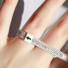 A close-up contextual photo showing the white plastic measuring tool in use on a person's finger. The adjustable belt is tightened around the base of the finger, with a black arrow pointing to the lettered scale to accurately determine ring size for jewellery purchases.
