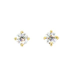 A product photo of two delicate moissanite earrings in 9k yellow gold sitting on a clear white background. The two small round-cut gems reflect multicoloured light and are held in place by four dainty golden claws.