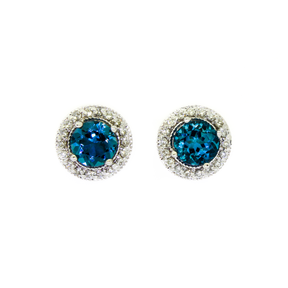 
            
                Load image into Gallery viewer, A product photo of a pair of white gold london blue topaz earrings sitting against a white background. The pair of circle-cut topaz stones are surrounded by thick frames of ornately detailed white gold and diamond detailing.
            
        