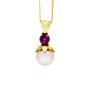 A product photo of a yellow gold rosaline pearl pendant with pink tourmaline detailing suspended by a yellow gold chain against a white background.