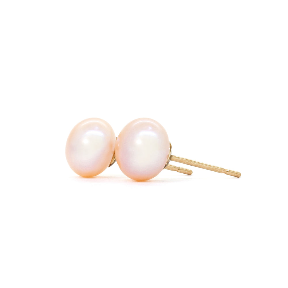 A product photo of simple peach-coloured pearl yellow gold earring studs on a white background.