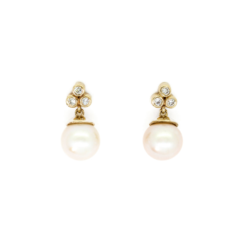A product photo of two white pearl yellow gold earring studs with trio diamond detailing above each pearl on a white background.