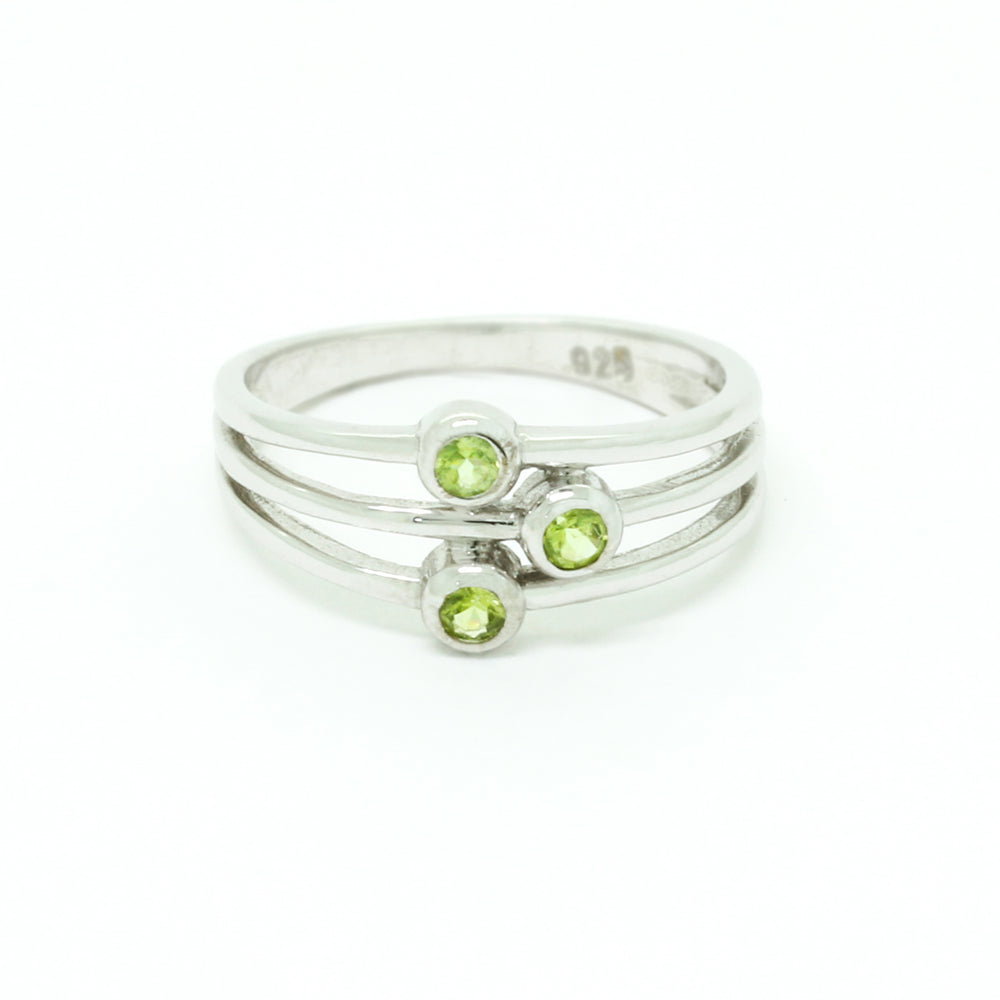 
            
                Load image into Gallery viewer, A product photo of a silver ring with 3 delicate bezel-set peridot stones sitting on a white background. The silver band is simple and smooth at the back before splitting into three prongs, each capped off with a delicate little peridot stone set within a silver frame. The prongs end at three different lengths, creating an interesting connecting line between the three stones. The peridot jewels are a shade of bright, pale green.
            
        