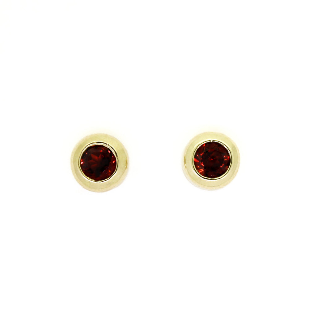 A product photo of 4mm Round Bezel-Set Garnet Earring Studs in 9k Yellow Gold sitting on a plain white background. The 2 garnet stones measure 4mm across and are deep red, reflecting sanguine hues across their multi-faceted edges, framed in a thick layer of yellow gold.