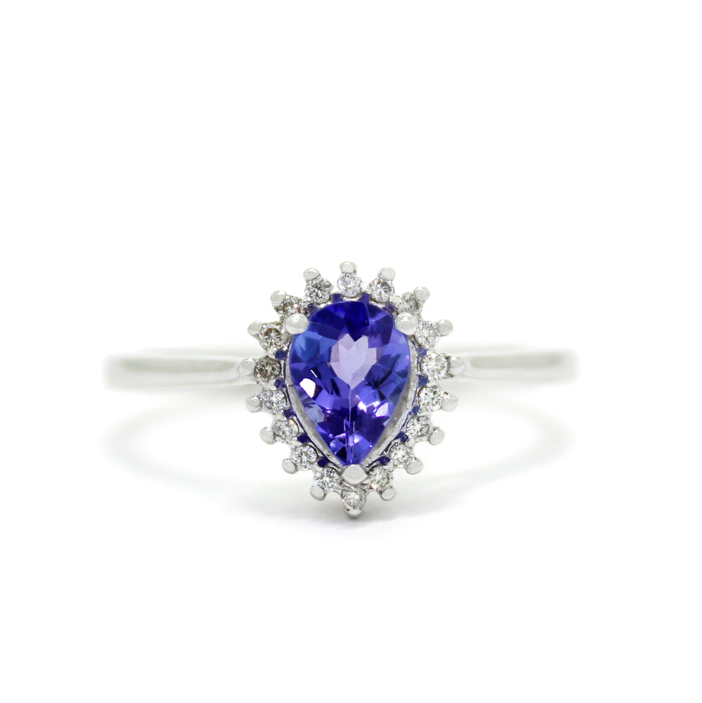 A product photo of a white gold tanzanite ring sitting on a white background. A flowery halo of diamond and white gold detailing frames the large, pear-shaped centre stone. The deep blue tanzanite reflects violet blue and indigo colours from its many edges.