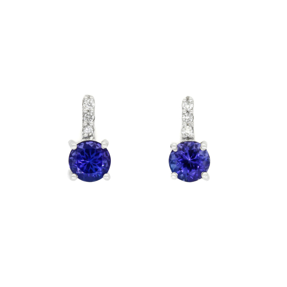 A product photo of white gold tanzanite stud earrings sitting on a white background. A golden strip connects the round stones to the studs, each strip adorned with 3 diamonds each. The deep blue tanzanite stones reflect violet blue and indigo light from their many edges.