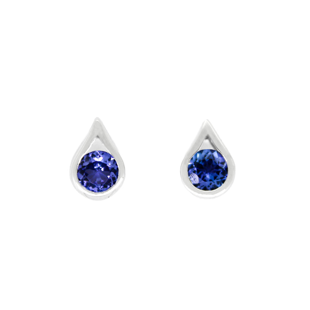 A product photo of white gold tanzanite stud earrings sitting on a white background. The round stones are encased by thick, white gold frames in the shapes of teardrops. The deep blue tanzanite stones reflect violet blue and indigo light from their many edges.