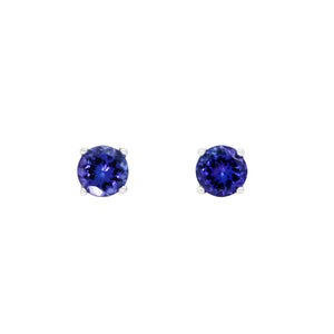 A product photo of white gold tanzanite stud earrings sitting on a white background. The round stones are held in place by 4 claws each, and reflect blue and indigo light from their many edges.