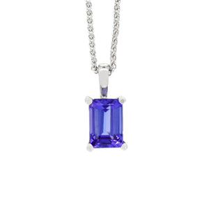 A product photo of a white gold tanzanite pendant suspended by a chain against a white background. The emerald-cut tanzanite stone is held in place by 4 golden claws, and reflects violet blue and indigo colours from its edges.