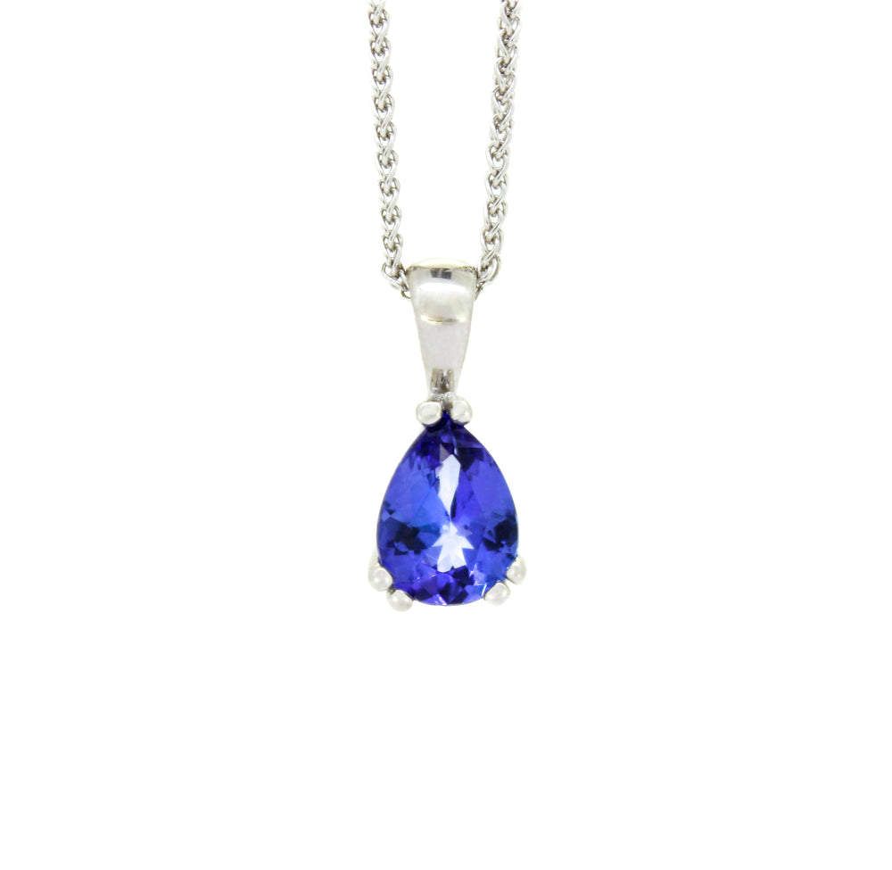 A product photo of a white gold tanzanite pendant suspended by a chain against a white background. The deep blue pear-shaped stone is held in place by three pairs of golden claws, and reflects violet blue and indigo colours from its many edges.