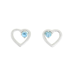 A product photo of two silver heart-shaped stud earrings sitting on a white background. A delicate, 2.5mm blue topaz stone is nestled in the top right corner of each heart-shaped frame.