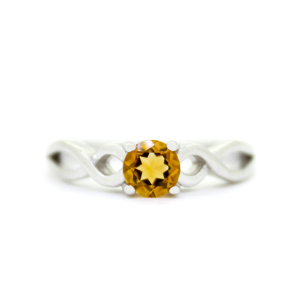 A product photo of an ornate silver ring with a citrine centre stone sitting on a white background. The silver band splits halfway along its length, becoming twisting and serpentine in appearance before meeting on either side of the dazzling sunny orange 5mm stone, which is held in place by 4 silver claws.