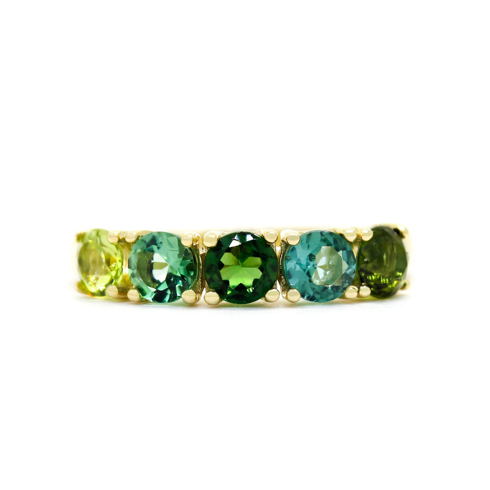 A product photo of a bold, multi-gemstone ring in 9k yellow gold – made up of 5 tourmaline jewels of various shades of green – sitting on a white background. From left to right, 4.5mm round-cut yellow-green, mint, emerald, sea and forest green tourmaline stones make up a bold statement piece.