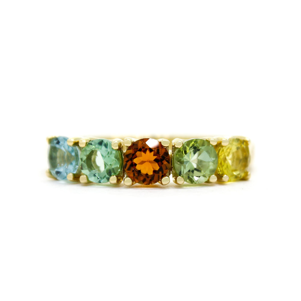 A product photo of a bold, multi-gemstone ring in 9k yellow gold – made up of 5 multi-coloured tourmaline jewels – sitting on a white background. From left to right, 4.5mm round-cut light blue, mint green, orange, pastel green and yellow tourmaline stones make up a bold statement piece.