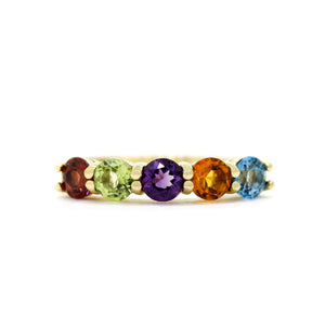 A product photo of a bold, multi-gemstone ring in 9k yellow gold – made up of rainbow-coloured jewels – sitting on a white background.