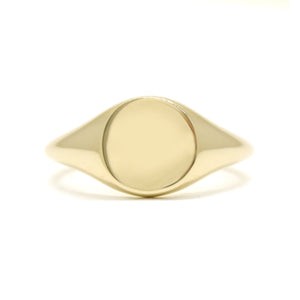 A product photo of a mens' signet ring made of 9k yellow gold. The face of the ring is a 10mm round flat circle that transitions to a thick rounded band.