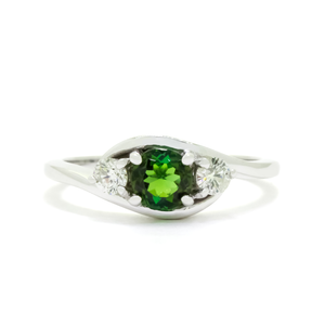 
            
                Load image into Gallery viewer, A product photo of a mystical tourmaline and diamond fantasy ring in solid 9k white gold on a white background. The deep, verdant-green tourmaline is held in place by 4 claws and reflects light off of its many facets, while the diamonds on either side are held by 3 each. The smooth white gold band curves elegantly, meeting at the top and bottom of the tourmaline and diamond arrangement. The green gemstone colour be a good emerald substitute.
            
        