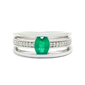 
            
                Load image into Gallery viewer, A product photo of a white gold trio-banded ring with diamond detailing and a natural emerald centre stone sitting on a white background. The top and bottom bands are smooth and minimalistic, hugging the top and bottom of the oval emerald centre stone, whilst the middle band (meeting on either side of the stone) is bejewelled with many tiny diamonds.
            
        