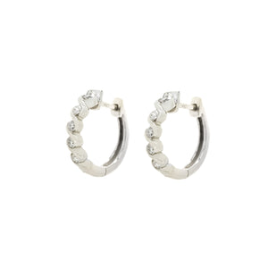 A product photo of two diamond huggies hoop earrings set in solid 9ct white gold suspended against a white background. The diamonds are set in looping waves of golden detailing, with each "wave" curling gently around a single white diamond to a total of 5.