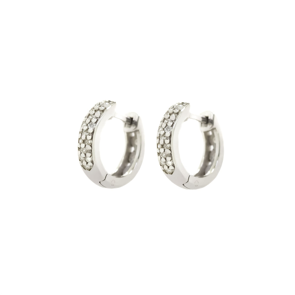 A product photo of two diamond huggies hoop earrings set in solid 9ct white gold suspended against a white background. The golden hoops are smooth and unblemished for the most part, with the front of each hoop decorated with 15 embedded white diamonds. They are arranged in an interesting pattern around the hoop, alternating between single and double diamond detailing in a vertical order.