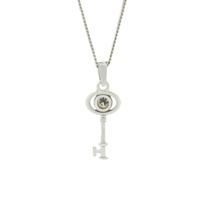 A product photo of a ceremonial diamond key pendant set in solid 9ct white gold. The design is dainty and left purposefully vague, so it may serve as a traditional 21st birthday present or as a key to something special to the wearer. The design consists of smooth and simple gold, with an oval-shaped loop framing a single round bezel-set diamond as the bow of the key, almost resembling an eye, while the rest of the key's design is simple and classic.