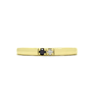 A product photo of a boldly minimalist wedding band made of solid 9k yellow gold sitting on a white background. The front is embedded with 2 tiny gemstones, one little black diamond, and one little white diamond. It is reminiscent of a ying and yang colour profile, symbolising the duality of marriage.