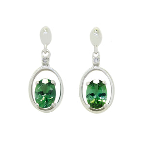
            
                Load image into Gallery viewer, A product photo of 7x5mm Oval Green Tourmaline &amp;amp; Diamond Earring Studs in 9k White Gold sitting on a plain white background. The stones are nestled at the bottom of golden oval hoops, with each being punctuated by a single diamond where they meet the stud. The tourmalines reflect forest green hues across their multi-faceted edges.
            
        
